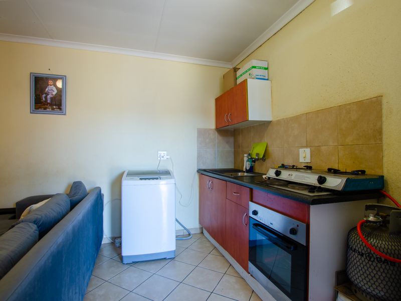 Compact kitchen area featuring built-in cabinetry, gas hob, oven, and tiled backsplash, with adjacent space for laundry appliances.