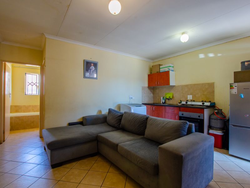 Open-plan living area featuring a compact kitchen with built-in cabinetry, gas hob, and oven, finished with tiled flooring throughout.