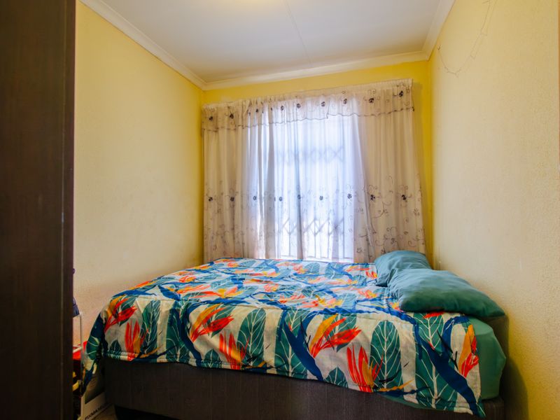 A compact bedroom featuring yellow walls, a security gate on the window, and cove cornicing.