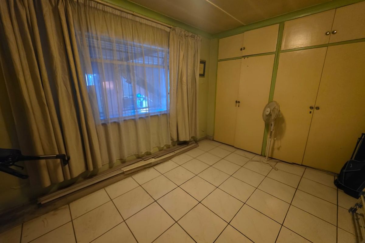 A bedroom featuring built-in cupboards, tiled flooring, and security bars on the window, offering a blank canvas for renovation.