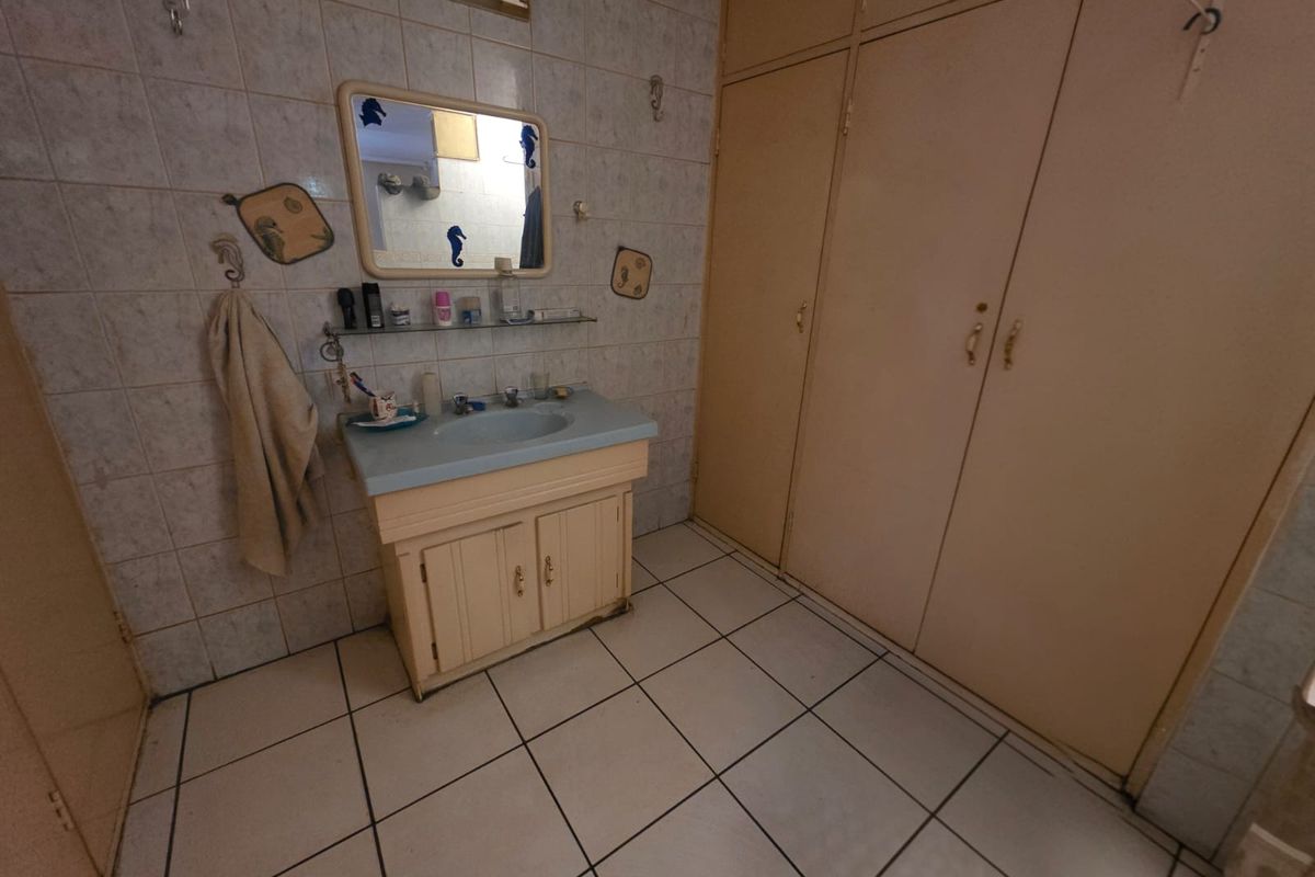 A dated bathroom featuring a vanity cabinet with a basin, built-in storage cupboards, and tiled wall and floor finishes.