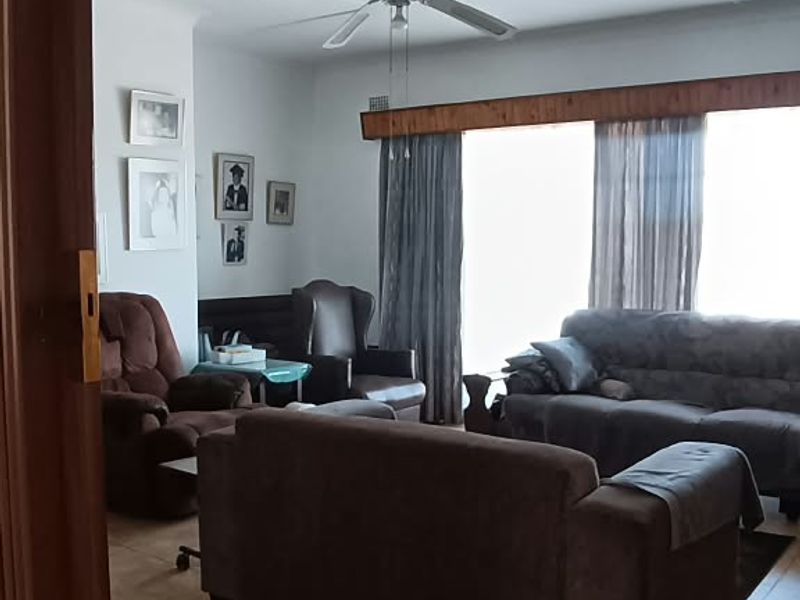 A living room featuring tiled flooring, a ceiling fan, and a wooden curtain pelmet, viewed from an adjacent doorway.