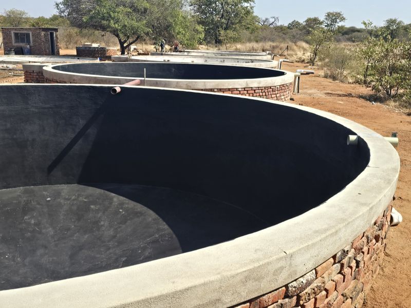 A series of circular brick-built water storage tanks with concrete coping and waterproof lining, situated in an open farm landscape.