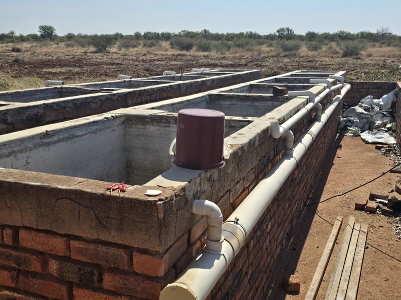 Outdoor brick masonry utility tanks with integrated PVC plumbing infrastructure, situated in a rural farm setting.