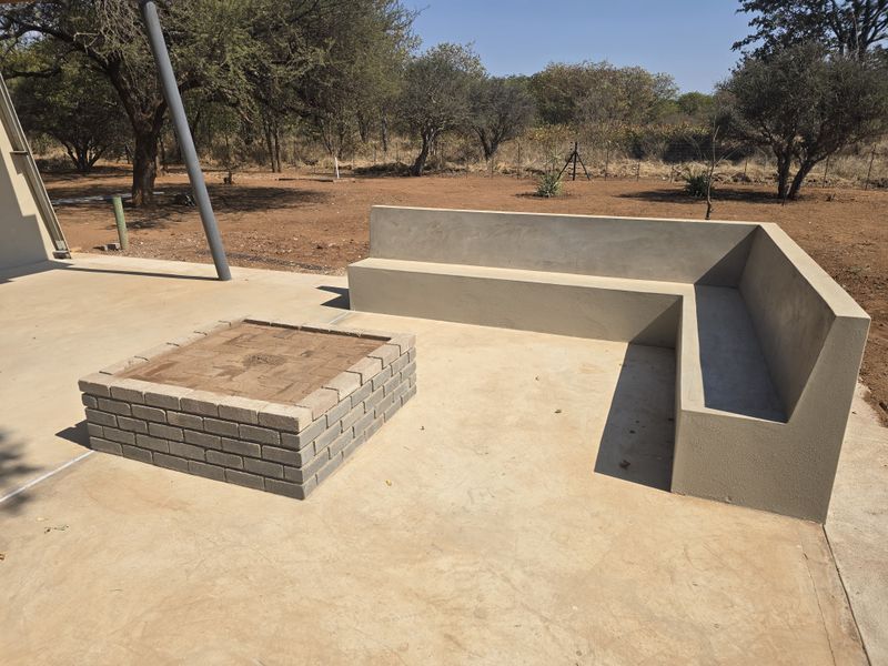 Outdoor patio area featuring a built-in concrete bench and a brick fire pit, set against a natural farm landscape.