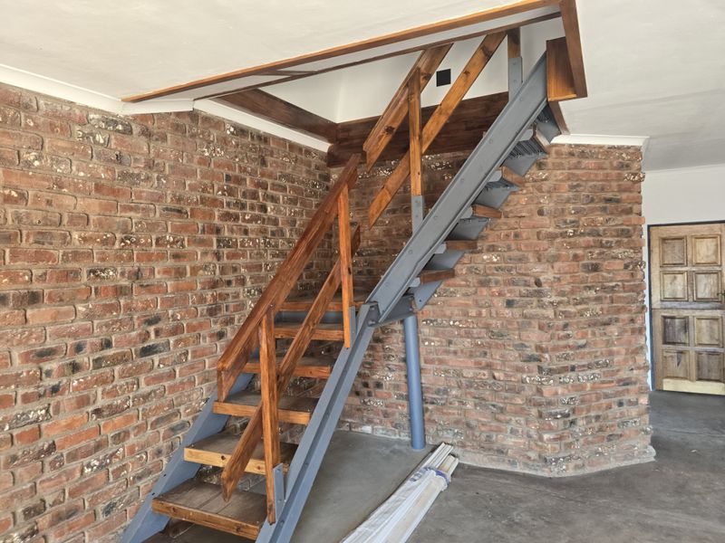 A spacious garage area featuring exposed brick walls and a sturdy steel and timber staircase leading to an upper level.