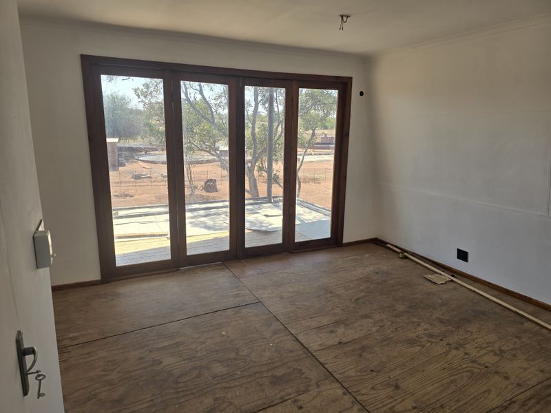An empty, unfinished living room featuring large wooden folding doors that open to an outdoor area, currently with exposed plywood subflooring.