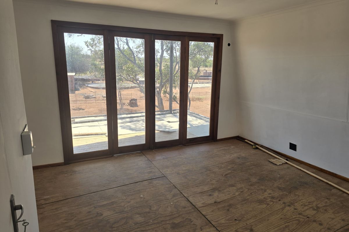 An empty, unfinished living room featuring large wooden folding doors that open to an outdoor area, currently with exposed plywood subflooring.