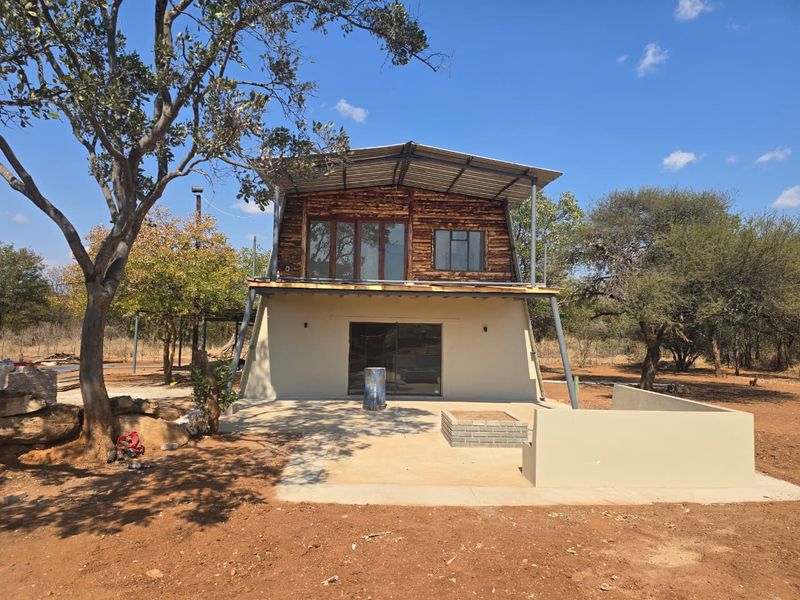 Rear view of a rustic farm dwelling featuring timber cladding, a corrugated metal roof, a concrete patio area, and a built-in brick fire pit.