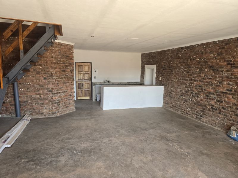 Open-plan area featuring exposed brick walls, a concrete floor, a built-in concrete bar counter, and a steel staircase leading to an upper level.