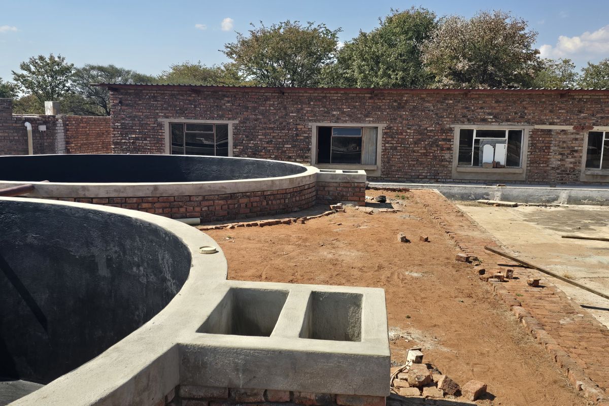 Rear exterior view of a farm property featuring exposed brick structures, circular concrete water tanks, and unfinished ground landscaping.