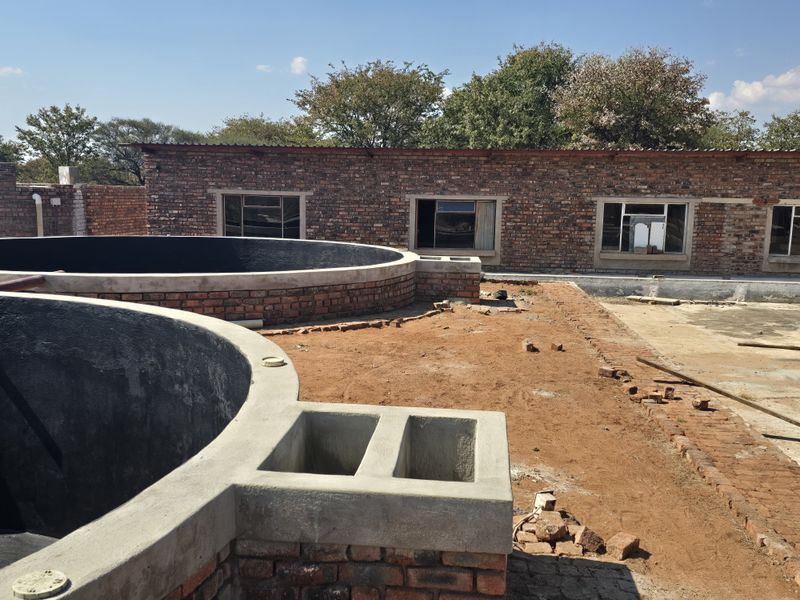 Rear exterior view of a farm property featuring exposed brick structures, circular concrete water tanks, and unfinished ground landscaping.