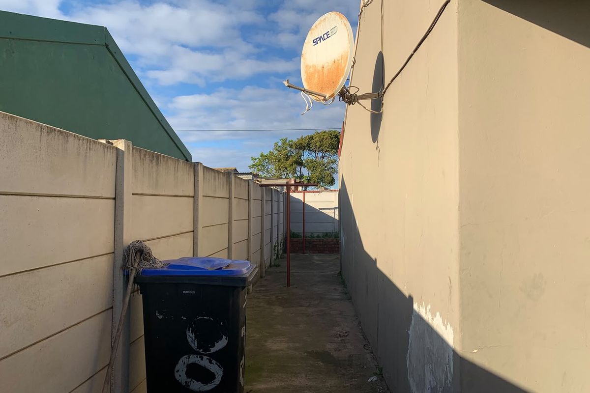 A narrow side passage or rear exterior area featuring concrete boundary walls, paved flooring, and a wall-mounted satellite dish.