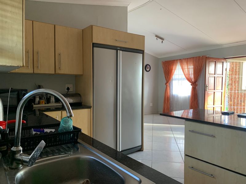 Open plan kitchen and living area featuring light wood cabinetry, granite countertops, and tiled flooring with direct access to an outdoor patio.