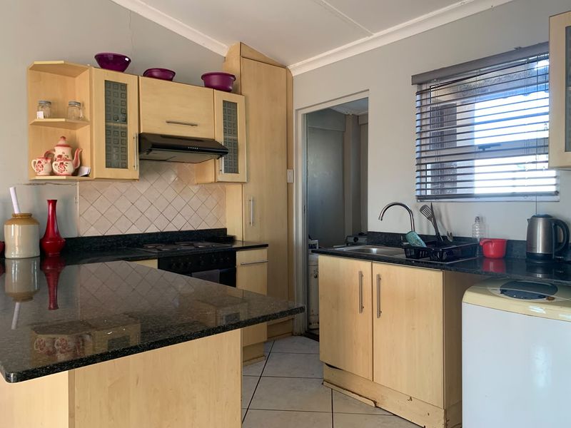 A functional kitchen featuring granite countertops, light wood veneer cabinetry, a built-in oven with extractor fan, and tiled flooring.