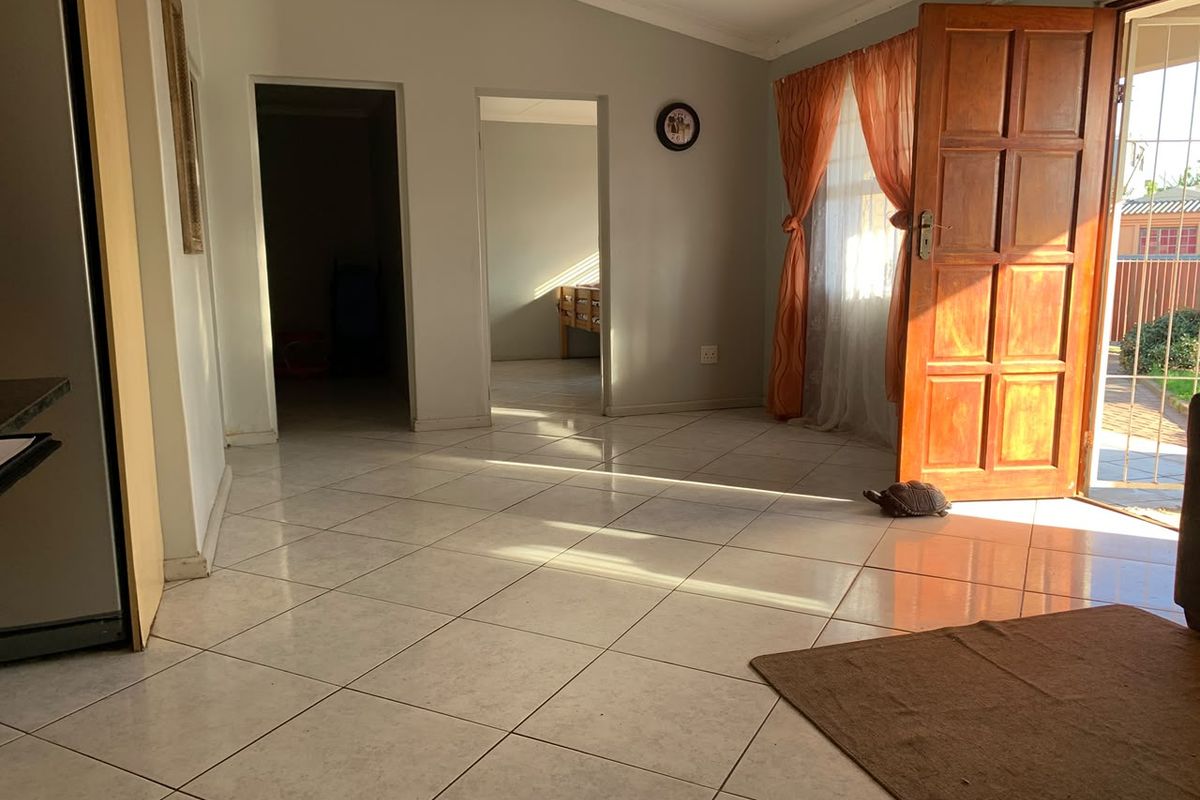 A bright, open-plan living area featuring neutral tiled flooring, coved cornicing, and direct access to the exterior through a timber panel door.