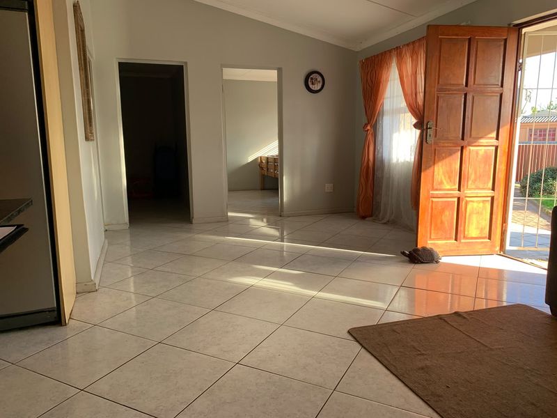A bright, open-plan living area featuring neutral tiled flooring, coved cornicing, and direct access to the exterior through a timber panel door.