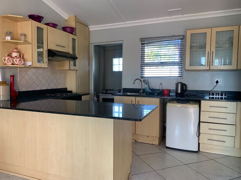 Functional kitchen featuring light wood cabinetry, dark granite countertops, built-in hob, extractor fan, and tiled flooring with a convenient breakfast nook.