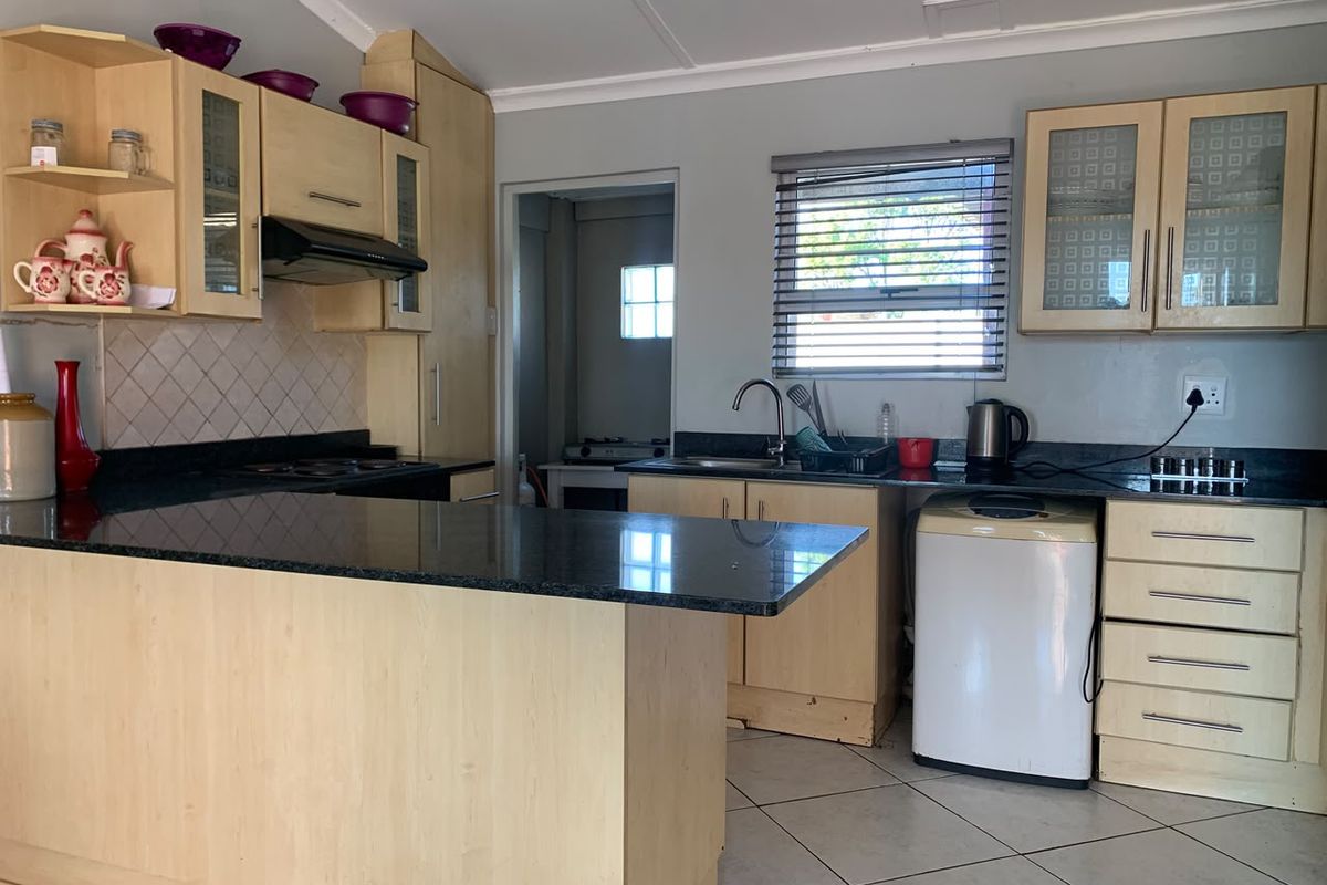 Functional kitchen featuring light wood cabinetry, dark granite countertops, built-in hob, extractor fan, and tiled flooring with a convenient breakfast nook.