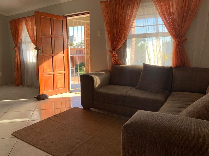 A sunlit living room featuring tiled flooring and direct access to the exterior through a timber door with a security gate.