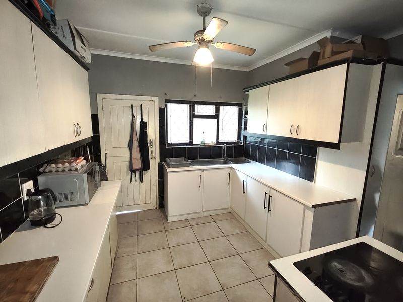 A functional kitchen featuring white built-in cabinetry, tiled backsplash, double sink, and ceramic floor tiles, offering a practical layout for daily meal preparation.