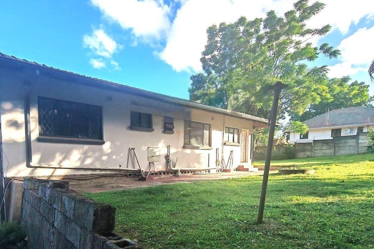 Rear view of the house featuring a concrete patio, lawn area, and brick boundary wall, showing signs of exterior wear and maintenance requirements.