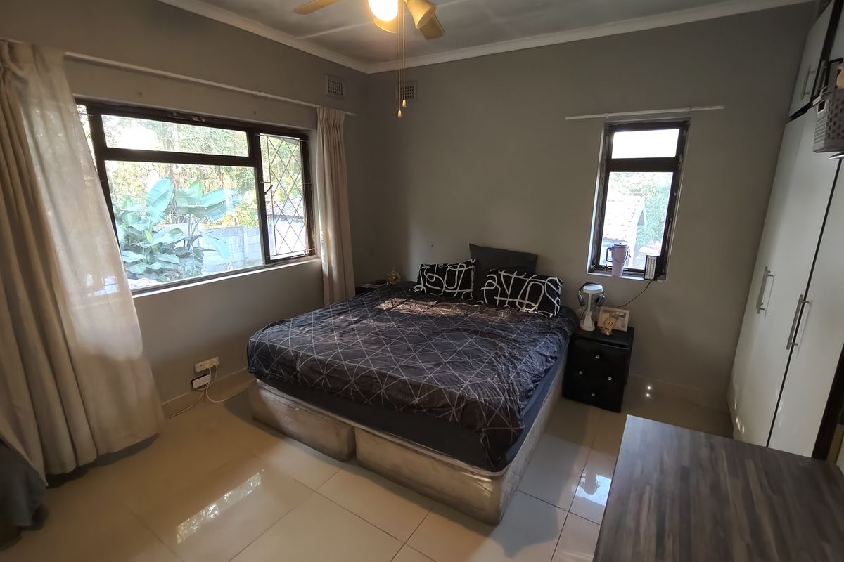 A functional bedroom featuring tiled flooring, built-in cupboards, and a ceiling fan, with natural light provided by multiple windows.