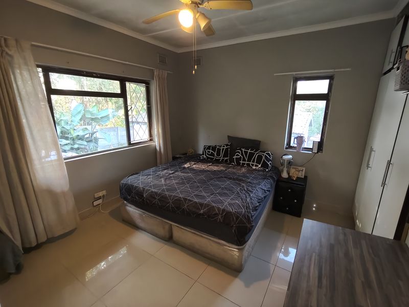 A functional bedroom featuring tiled flooring, built-in cupboards, and a ceiling fan, with natural light provided by multiple windows.