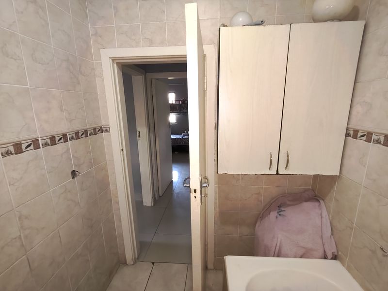 A dated bathroom featuring wall-to-wall tiling, a wall-mounted vanity cabinet, and a washbasin, requiring cosmetic updates to modernize the space.