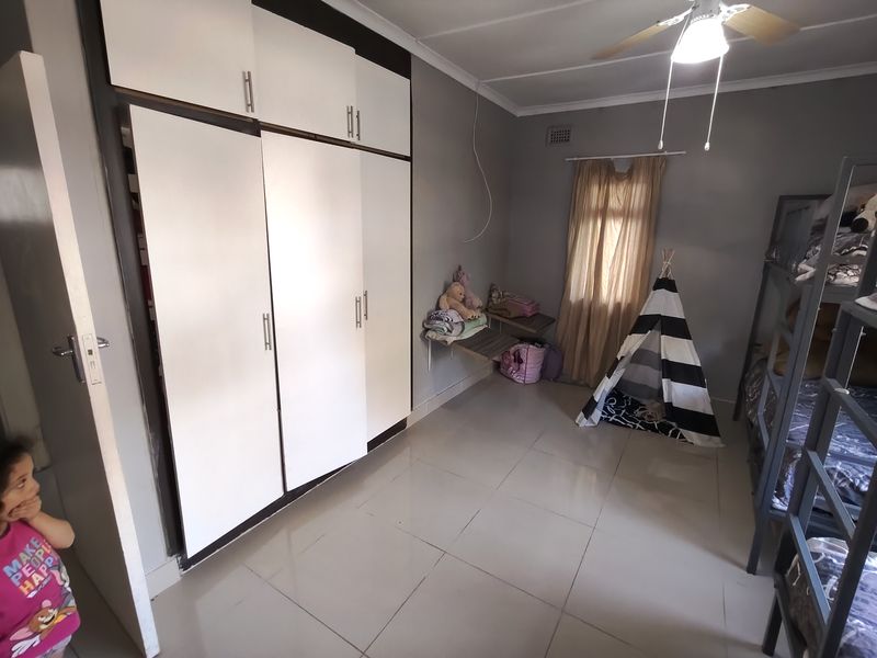 A bedroom featuring built-in cupboards, tiled flooring, and a ceiling fan. The space offers functional storage and neutral wall finishes.