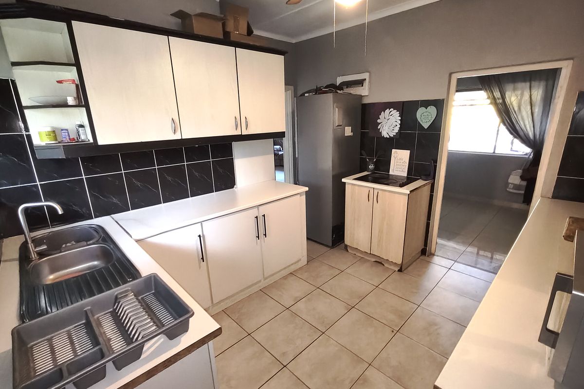Functional kitchen featuring built-in cabinetry, double bowl stainless steel sink, tiled backsplash, and ceramic floor tiles with a ceiling fan.