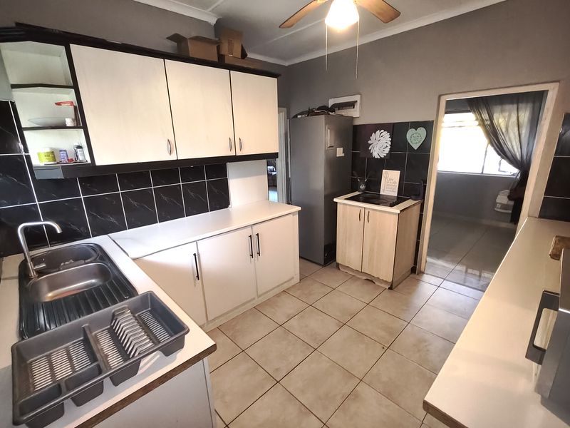 Functional kitchen featuring built-in cabinetry, double bowl stainless steel sink, tiled backsplash, and ceramic floor tiles with a ceiling fan.