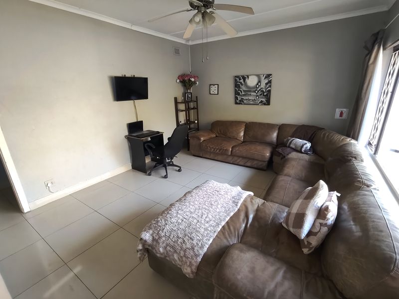 A spacious living room featuring neutral wall tones, tiled flooring, and a ceiling fan, providing a comfortable and functional area for relaxation.