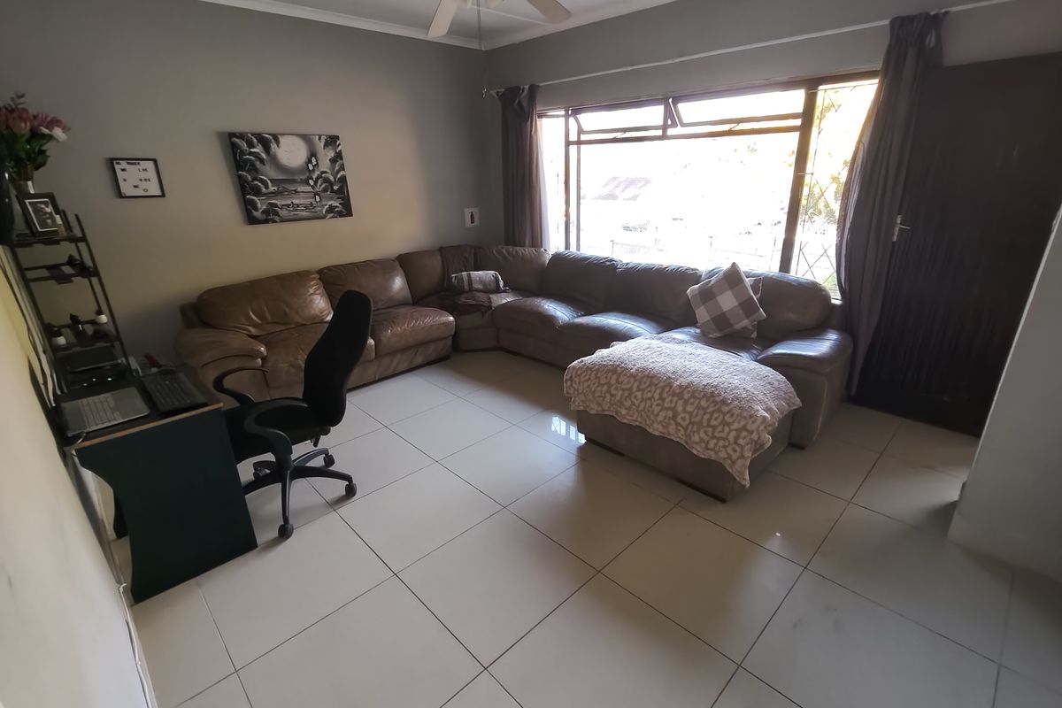 A spacious living room featuring large windows for natural light, tiled flooring, and a ceiling fan.