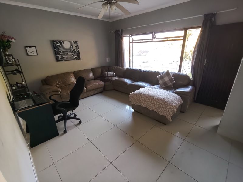 A spacious living room featuring large windows for natural light, tiled flooring, and a ceiling fan.