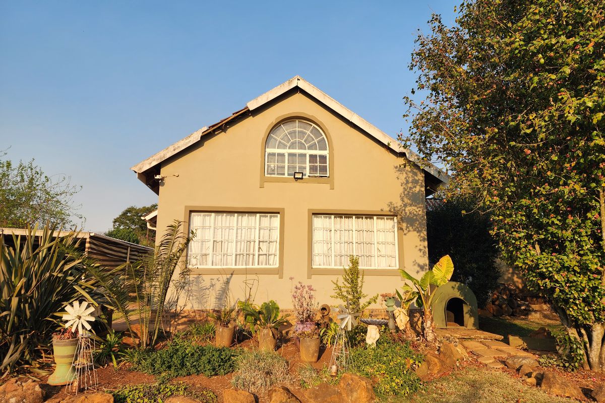Rear view of a residential house featuring a gabled roof, arched upper window, and landscaped garden area.