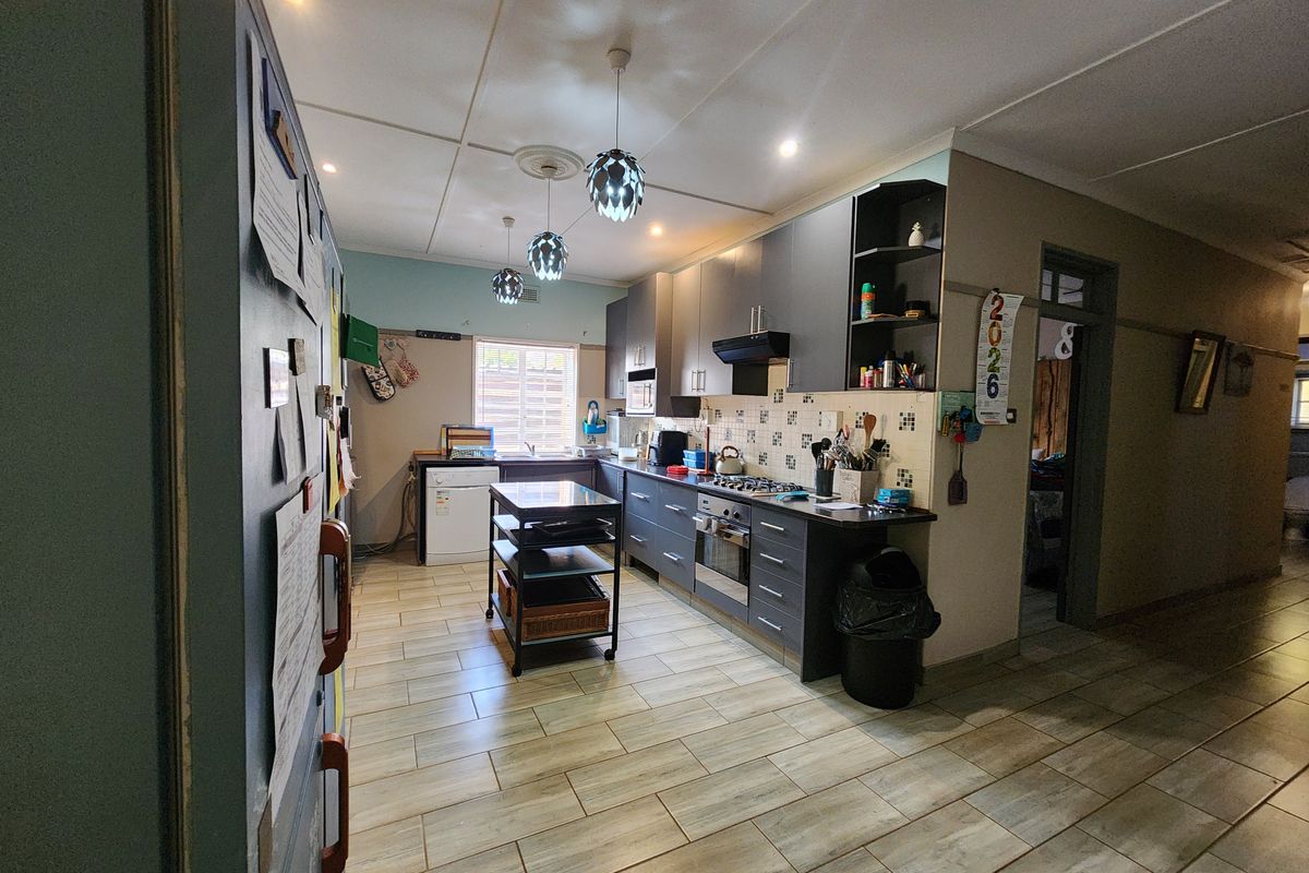 A functional kitchen featuring dark cabinetry, a gas hob, built-in oven, extractor fan, and tiled flooring with modern pendant lighting.