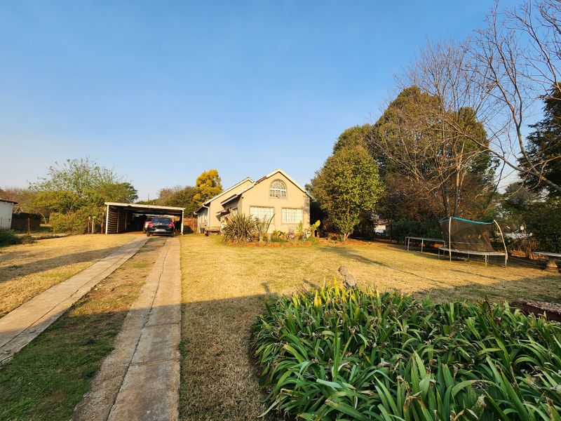 Front view of the property featuring a concrete driveway, attached carport, and a well-established garden area.
