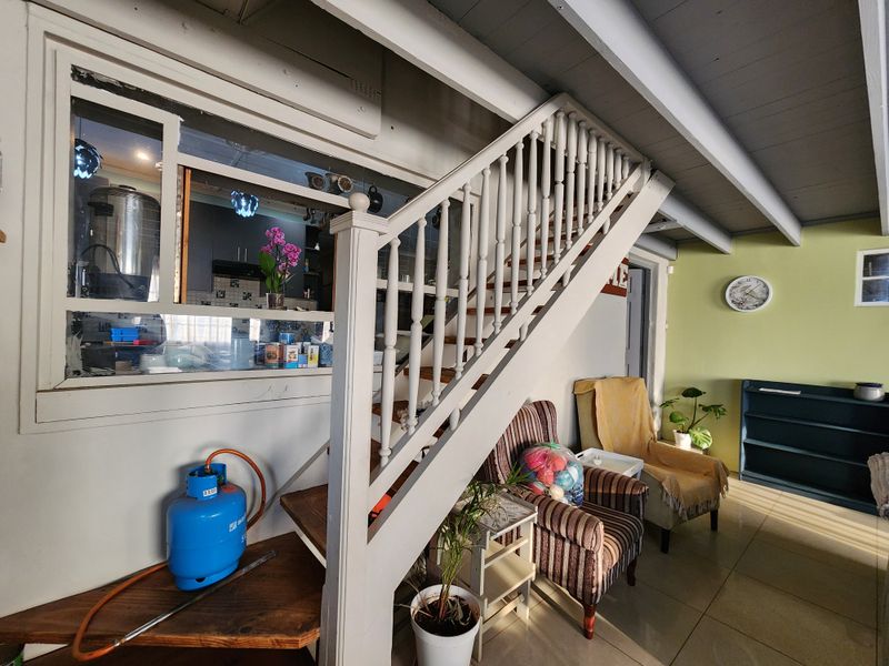 Living area featuring a timber staircase with balustrade, exposed ceiling beams, and an internal window partition looking into the kitchen area.