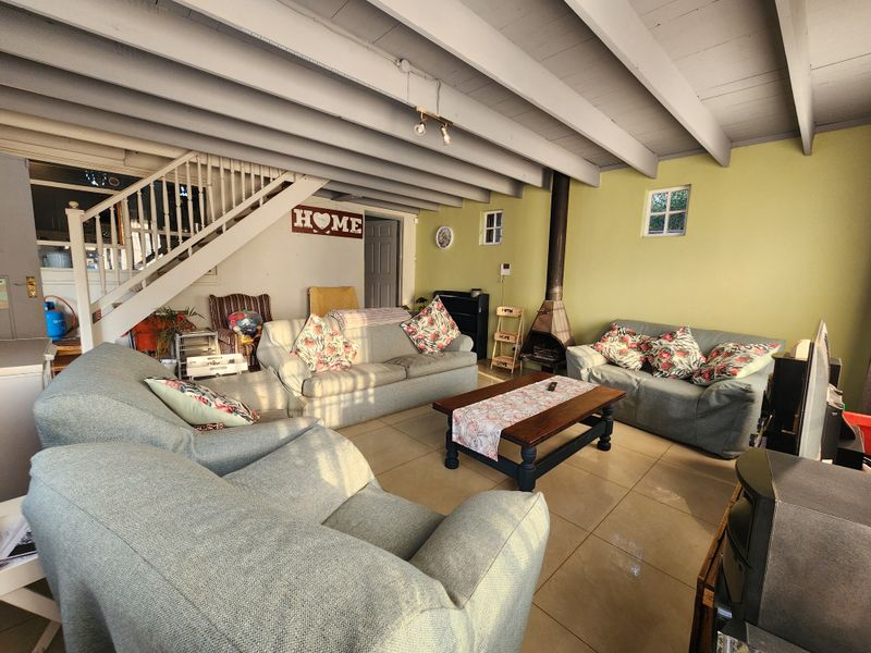 Spacious living room featuring exposed beam ceilings, tiled flooring, and a characterful freestanding fireplace, with an integrated staircase leading to the upper level.