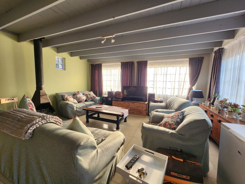 A comfortable living room featuring an exposed beam ceiling, tiled flooring, and a prominent freestanding fireplace.