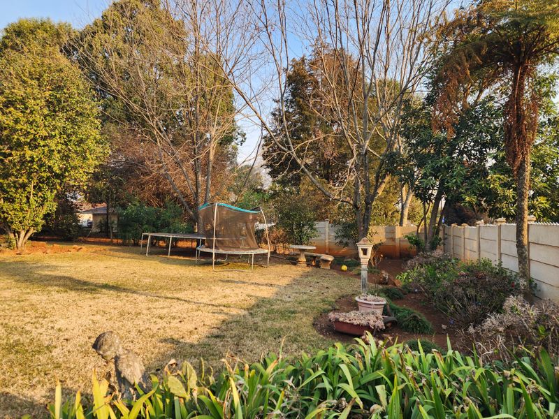 A spacious backyard garden featuring mature trees, established landscaping, and a secure precast concrete boundary wall.