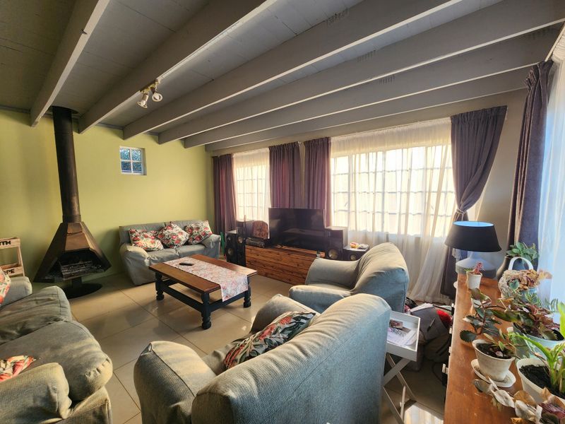 Spacious living room featuring an exposed beam ceiling, tiled flooring, and a prominent freestanding fireplace, offering a comfortable and inviting atmosphere.