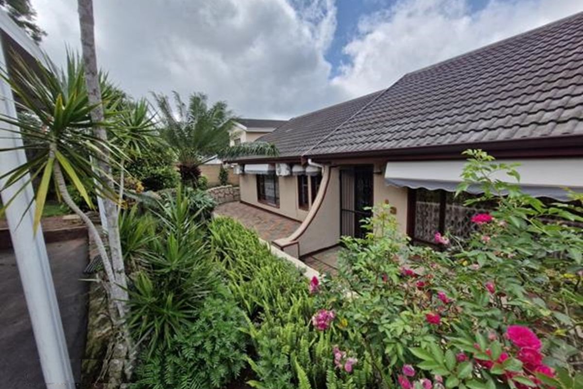 A view of the rear exterior of the house featuring a paved patio area, landscaped garden, and tiled roof.