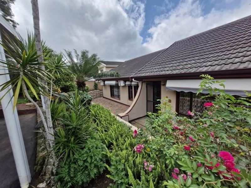 A view of the rear exterior of the house featuring a paved patio area, landscaped garden, and tiled roof.