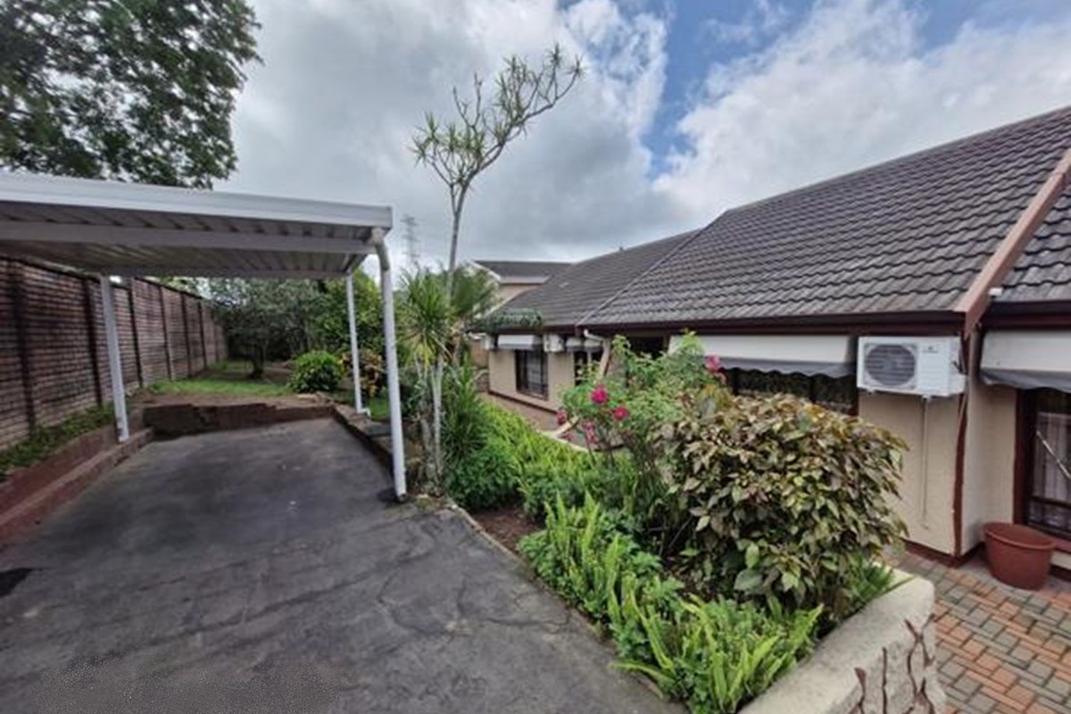 Rear exterior view featuring a carport, paved driveway, and established garden beds alongside the main dwelling structure.