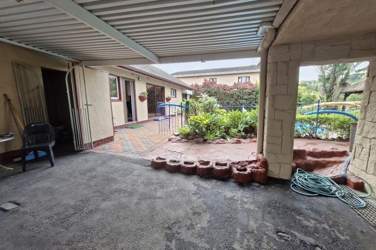 A covered outdoor patio area featuring paved flooring, a stone pillar, and direct access to the garden and pool area.
