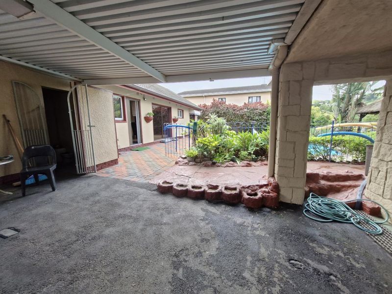 A covered outdoor patio area featuring paved flooring, a stone pillar, and direct access to the garden and pool area.