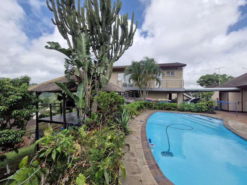 Outdoor pool area featuring a swimming pool, stone paving, and a thatched gazebo, set against the rear elevation of the house.
