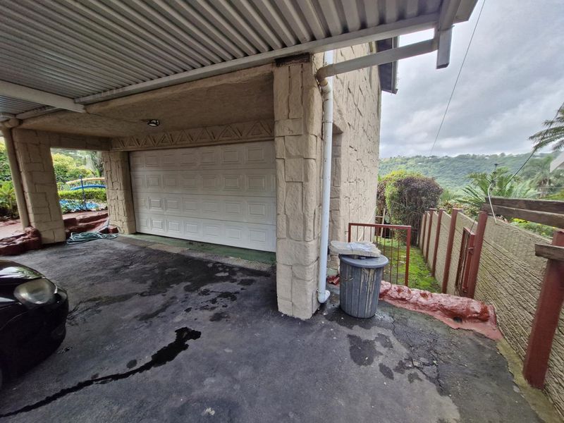 A covered carport area featuring a sectional garage door, stone-clad support pillars, and an asphalt driveway with views of the surrounding landscape.